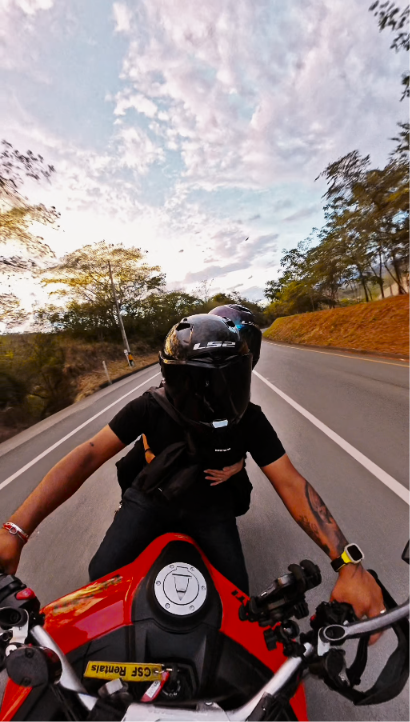 Dos personas con casco sobre una motocicleta roja en una carretera rodeada de árboles.