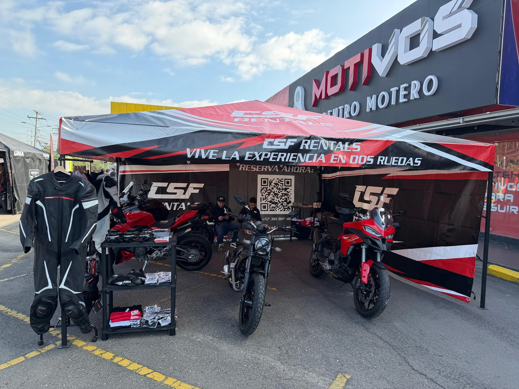 Carpa roja, negra y blanca de CSF Rentals instalada al aire libre, con motocicletas y un panel con código QR.