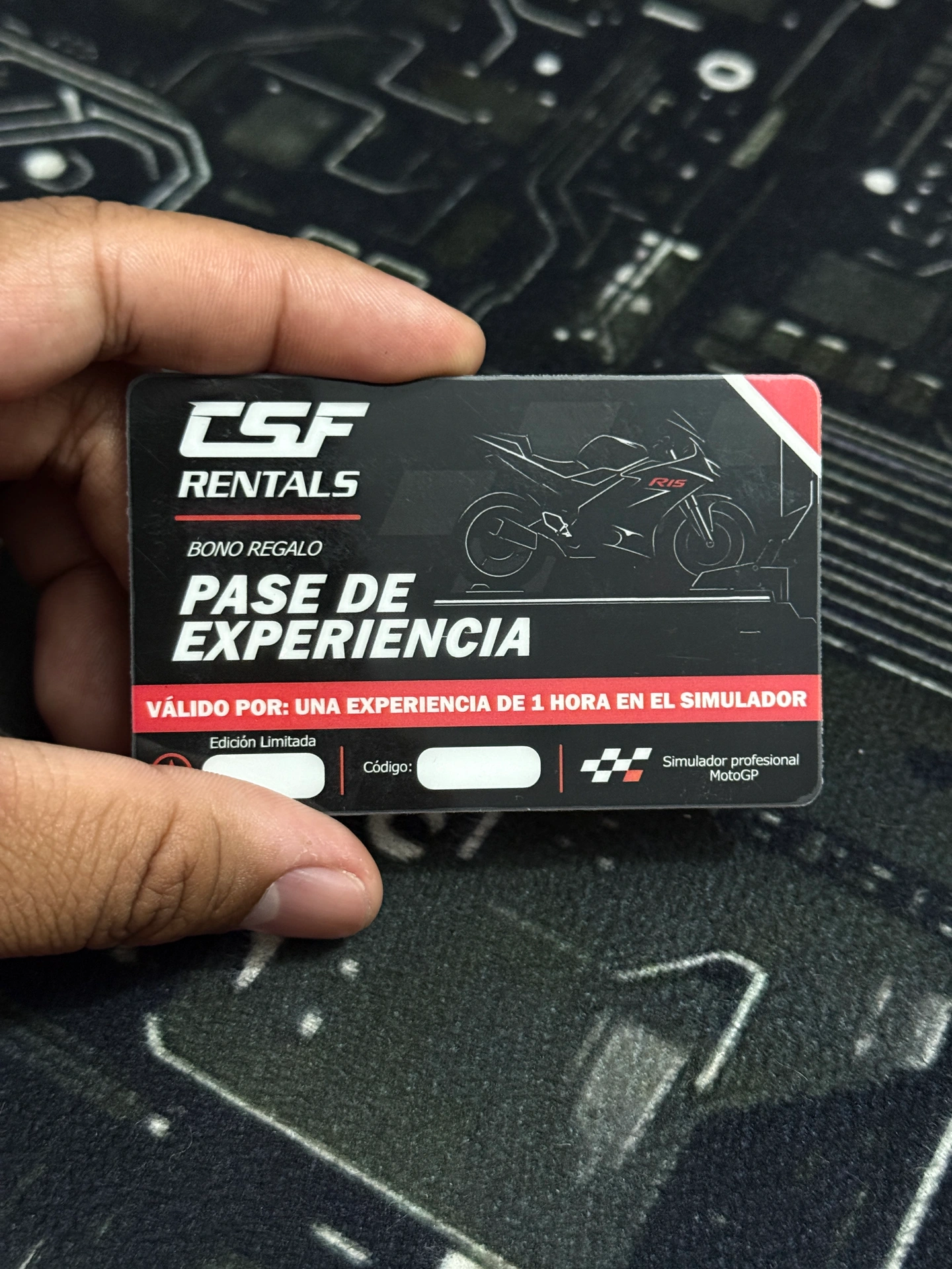 Mano sosteniendo una tarjeta negra y roja de CSF Rentals con el texto «Pase de experiencia» para una hora de simulador.